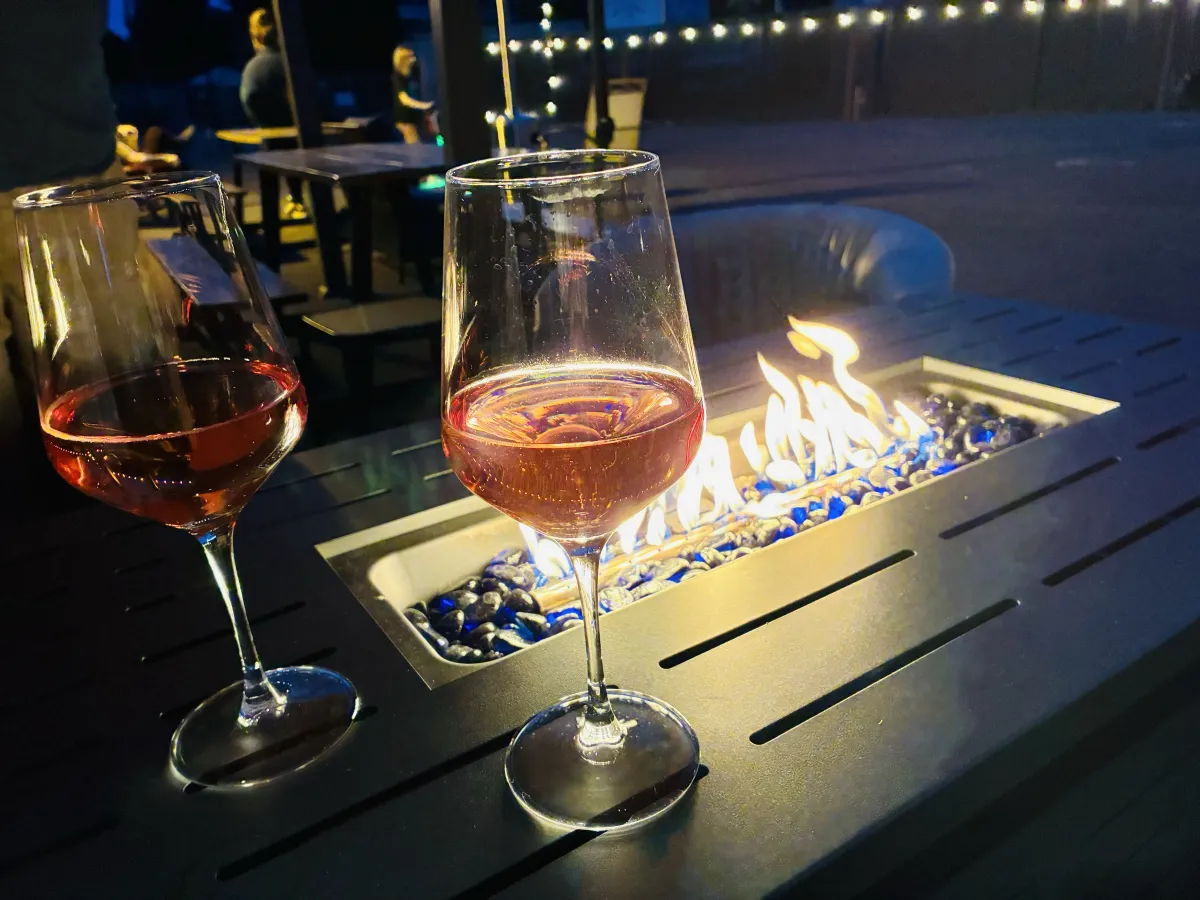 Two glasses of rosé by a lit fire table on the patio at dusk