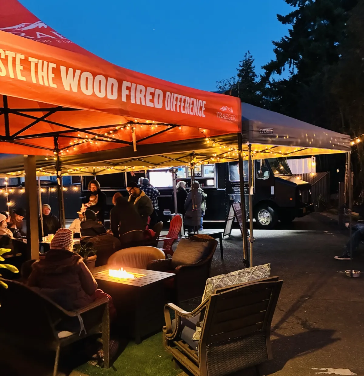 Evening on the patio — guests around a fire table under string lights by the food carts